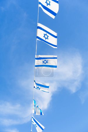 Photo for Israel flag bunting fluttering against a backdrop of blue sky with white clouds on Independence Day of Israel. - Royalty Free Image