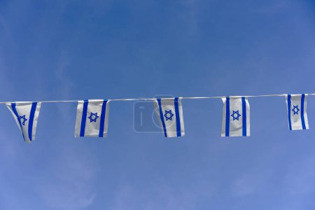 Israel flag bunting fluttering against a backdrop of blue sky with white clouds on Independence Day of Israel.