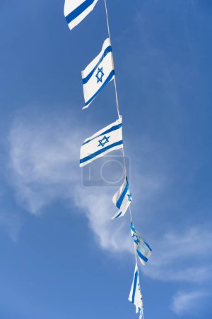 Photo for Israeli blue and white flag bunting fluttering against a backdrop of blue sky with white clouds on Independence Day of Israel. Perfect for projects related to Israeli culture and celebrations. - Royalty Free Image