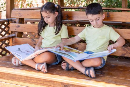 Sommerlicher Lesegenuss. Junge und Mädchen vertiefen sich in Bücher in der Straßenbibliothek. Kleine Kinder versinken in Büchern in Straßenbücherei auf Holzbank.