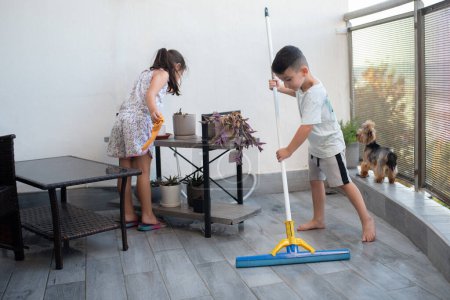 Photo for Efficient Balcony Cleaning: Boy Washing Floor, Girl Wipes Table, Playful Dog Adds Joy. - Royalty Free Image