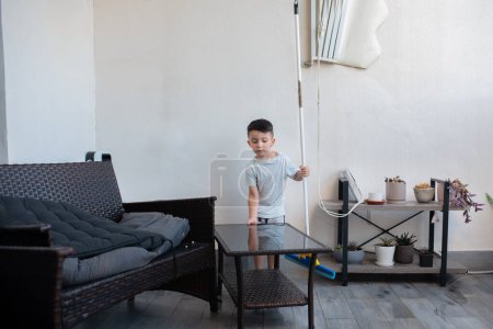Photo for Boy washing floor with mopping stick in balcony of modern apartment. Happy child cleaning at home terrace with the floor squeegee. - Royalty Free Image