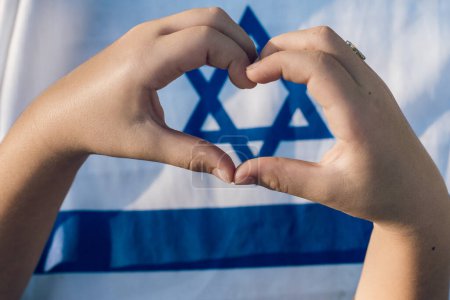 Heartfelt Gesture. Child Forms a Heart with Hands, Framing Magen David On Israeli Flag - Love Israel, Unity, Jewish Identity, Patriotism Symbol.