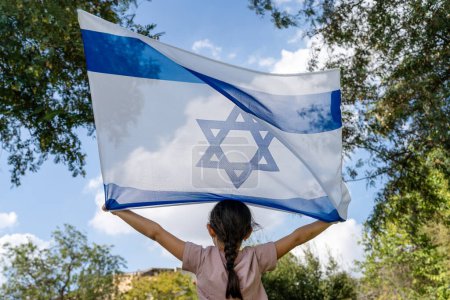 Vista posterior del niño con bandera israelí en el cielo azul, nubes y antecedentes de la naturaleza.