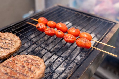 Close-up of a barbecue grill with charred tomato skewers and grilled veggie burgers, showcasing a healthy, antihistamine diet option and trending meat substitutes for modern cuisine.