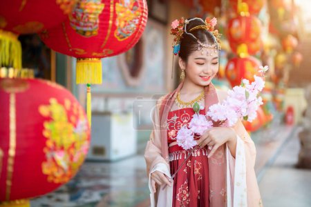 Portrait Lächeln Nettes kleines asiatisches Mädchen in chinesischen Kostümen und halten rosa Blumenzweige für das chinesische Neujahrsfest feiern die Kultur des Porzellans am chinesischen Schrein Öffentliche Plätze in Thailand