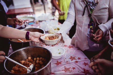 Photo for The hand of the wanderer extends to receive food from donations. With volunteers scooping food: the idea of helping with hunger - Royalty Free Image