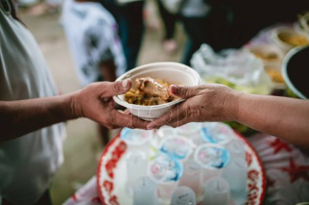 Photo for The hand of the wanderer extends to receive food from donations. With volunteers scooping food: the idea of helping with hunger - Royalty Free Image
