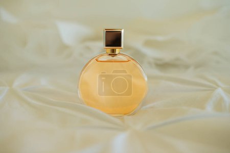 Photo for Round glass perfume bottle filled with gold perfume and gold cap on white silk background - Royalty Free Image