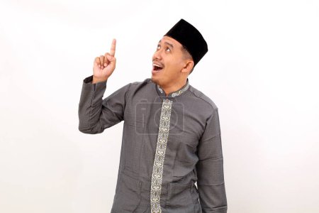 Photo for Surprised asian muslim man standing while pointing something above him. Isolated on white background - Royalty Free Image
