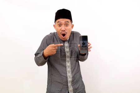 Photo for Asian muslim man presenting and pointing his cell phone screen. Isolated on white background - Royalty Free Image