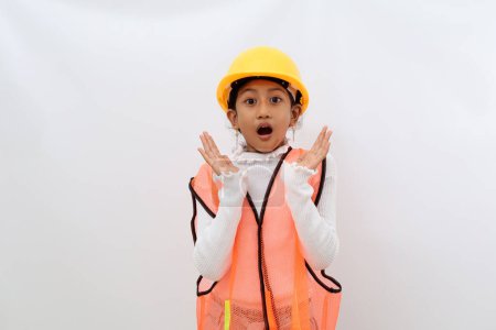 Photo for Shocked Asian little girl in the construction helmet as an engineer standing while looking at the camera. Isolated on white with copyspace - Royalty Free Image