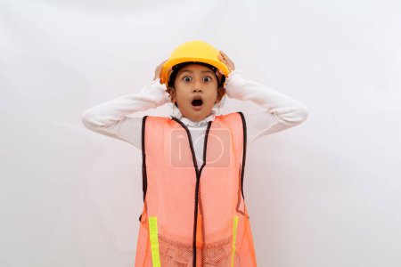 Photo for Shocked Asian little girl in the construction helmet as an engineer standing while holding her head. Isolated on white - Royalty Free Image