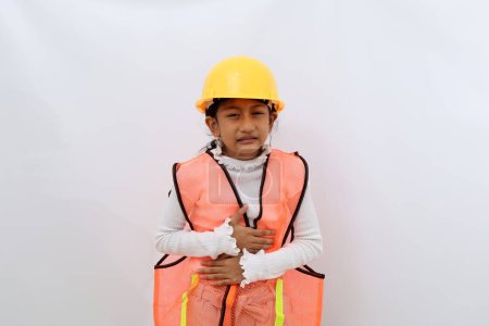 Foto de Asian little girl in the construction helmet as an engineer suffering from stomach ache. Isolated on white - Imagen libre de derechos