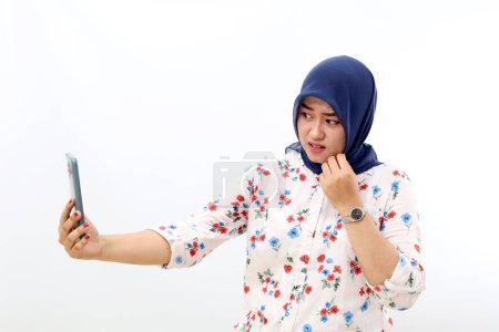 Photo for Scared asian muslim woman standing while watching video on her cell phone. Isolated on white - Royalty Free Image
