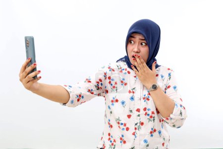 Téléchargez les photos : Shocked asian muslim woman standing while getting a news from her phone. Isolated on white - en image libre de droit
