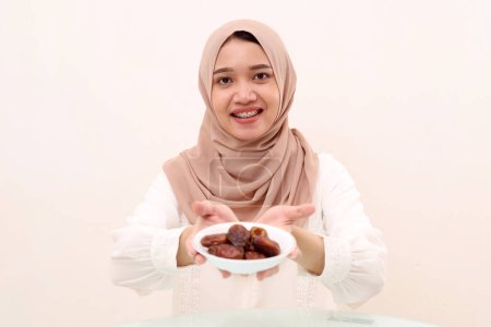 Young asian muslim woman holding a plate of date palm fruit. Selective focus. Ramadhan concept.
