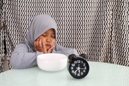 Photo for Sleepy Asian muslim little girl waiting for breaking her fast. Ramadhan concept - Royalty Free Image