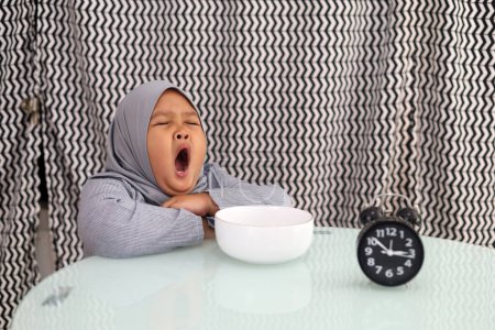 Photo for Asian muslim little girl feelling sleepy when waiting for breaking her fast. Ramadhan concept - Royalty Free Image