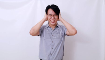Stressed asian man covering his ears from loud noises. Isolated on white