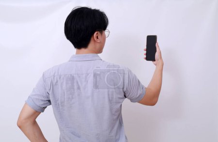 Téléchargez les photos : Vue arrière photo de l'homme asiatique tenant un téléphone portable. Isolé sur blanc - en image libre de droit