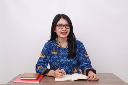 Téléchargez les photos : Asiatique femme portant batik korpri, indonésien traditionnel travailleur uniforme dans bureau bureau - en image libre de droit