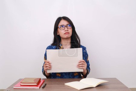 Photo for Asian female in batik korpri, indonesian worker uniform showing a blank paper while thinking an idea - Royalty Free Image