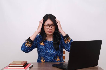 Photo for Stressed Asian female in batik korpri, indonesian traditional uniform having headache while working - Royalty Free Image