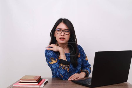 Téléchargez les photos : Asiatique femelle en batik korpri, indonésien uniforme traditionnel ayant des douleurs à l'épaule tout en travaillant - en image libre de droit