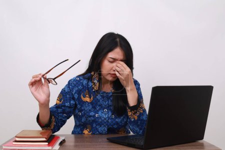 Photo for Tired Asian female in batik korpri, indonesian traditional uniform holding her head while working - Royalty Free Image