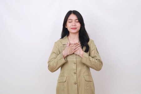 Photo for Relieved young indonesian civil servant employee holding her chest while closing her eyes - Royalty Free Image