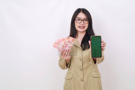 Photo for Pretty young asian teacher holding Indonesian banknotes while showing blank cell phone display - Royalty Free Image