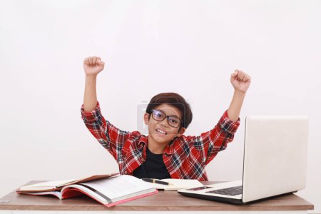 Photo for Asian student raising and clenching his hands while studying with books and laptop. Isolated - Royalty Free Image