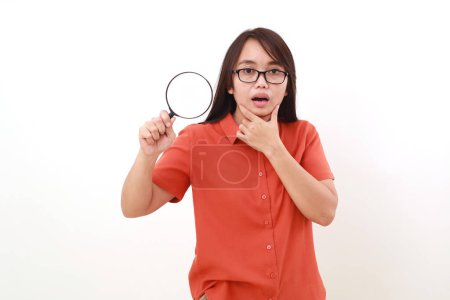 Photo for Asian woman showing her suspicion face expression while holding magnifying glass. Isolated on white - Royalty Free Image