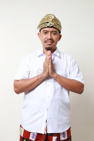 Téléchargez les photos : Homme asiatique en costume traditionnel balinais debout avec geste de main accueillant ou namaste. Isolé sur fond blanc - en image libre de droit