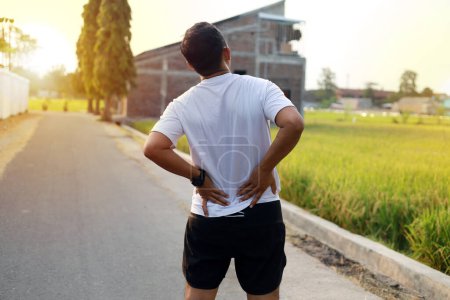 Téléchargez les photos : Asiatique homme avec mal de dos pendant faire de l'exercice extérieur - en image libre de droit