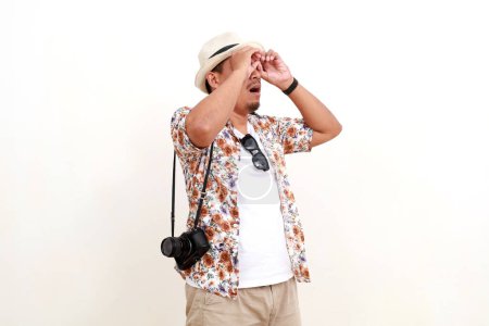 Photo for Asian man traveler standing while using his hands for binoculars looking sideways. Isolated on white background with copyspace - Royalty Free Image