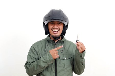 Téléchargez les photos : Heureux homme asiatique portant une veste et un casque tout en tenant une clé de moto. Isolé sur fond blanc - en image libre de droit