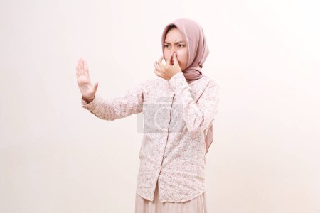 Téléchargez les photos : Jeune femme musulmane asiatique couvrant son nez tout en montrant stop geste de la main. Concept de mauvaise odeur - en image libre de droit