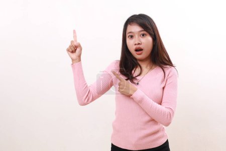 Photo for Wow shocked young asian girl pointing above while looking at the camera and open mouth. Advertisement and promotional concept. Isolated on white background - Royalty Free Image