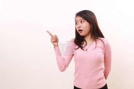 Photo for Wow expression of young asian girl pointing sideways while looking at empty space. Advertisement and promotional concept. Isolated on white background - Royalty Free Image