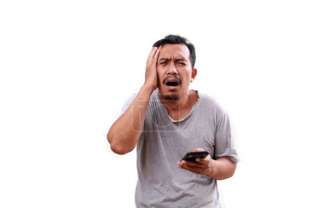 Photo for Stressed frustrated poor asian man holding head while carrying cell phone. Isolated on white with copyspace - Royalty Free Image