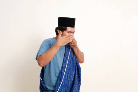 Asian muslim boy standing while covering his nose. Bad smell concept