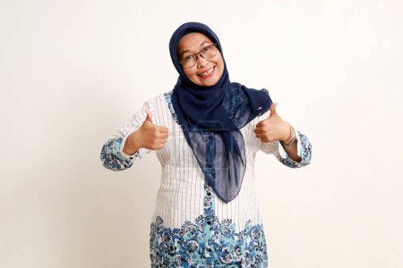 Asiatische ältere muslimische Frau zeigt Daumen hoch mit glücklichem Gesichtsausdruck