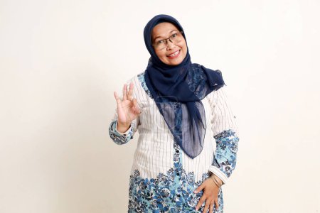 Glücklich asiatisch ältere muslimische Frau stehend, während sie okay Handgeste zeigt