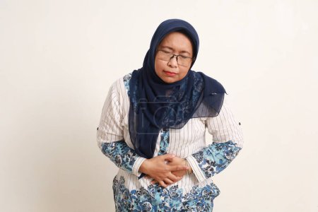 Asiática anciana sufriendo de dolor de estómago, mano sosteniendo su vientre