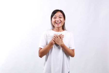 Bild einer überraschten und dankbaren jungen Frau, die ein Geschenk entgegennimmt, die Hände auf der Brust hält, mit geschmeicheltem Lächeln Danke sagt, gelobt wird, vor weißem Hintergrund steht.