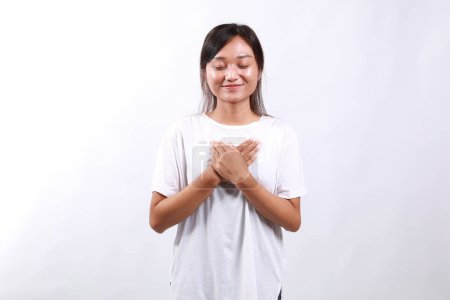 Asiatique jeune femme souriant avec les mains sur la poitrine avec les yeux fermés et geste reconnaissant sur fond blanc, se sent soulagé