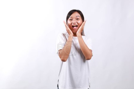 Young cheerful asian woman look with surprised face at camera, react to awesome good news, smiling and cheering, standing against white background