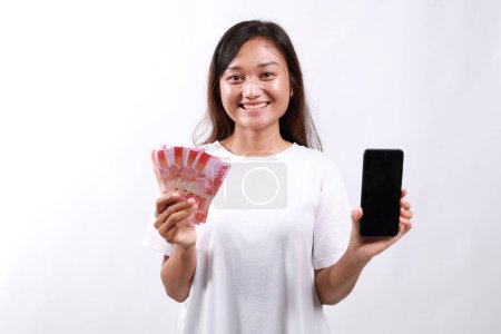 Jeune femme asiatique montrant écran de téléphone mobile et de l'argent, de l'argent, concept de microcrédit et de prêts bancaires, debout sur fond blanc